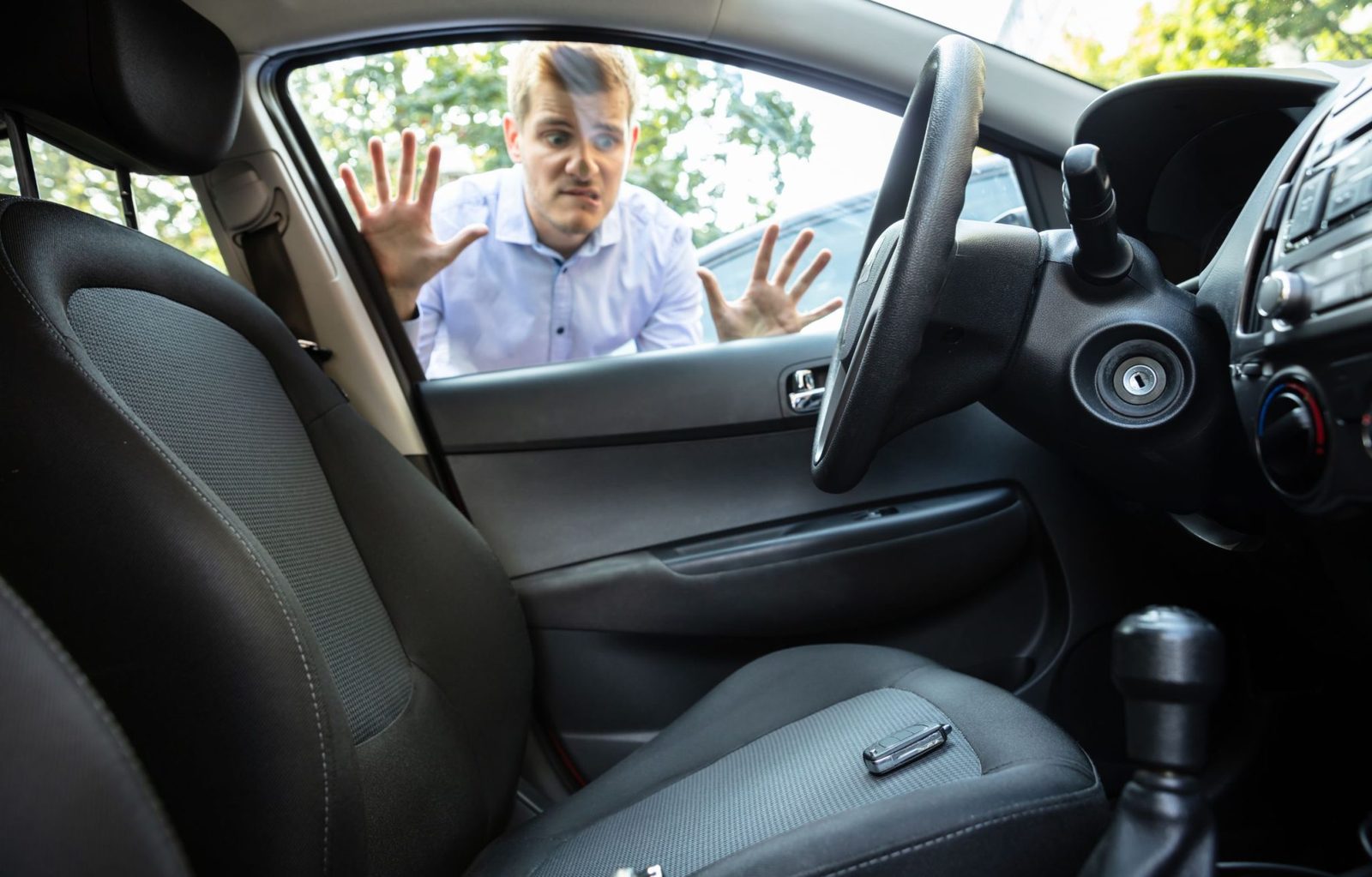 Driver looking through a car window at keys left sitting on the front seat